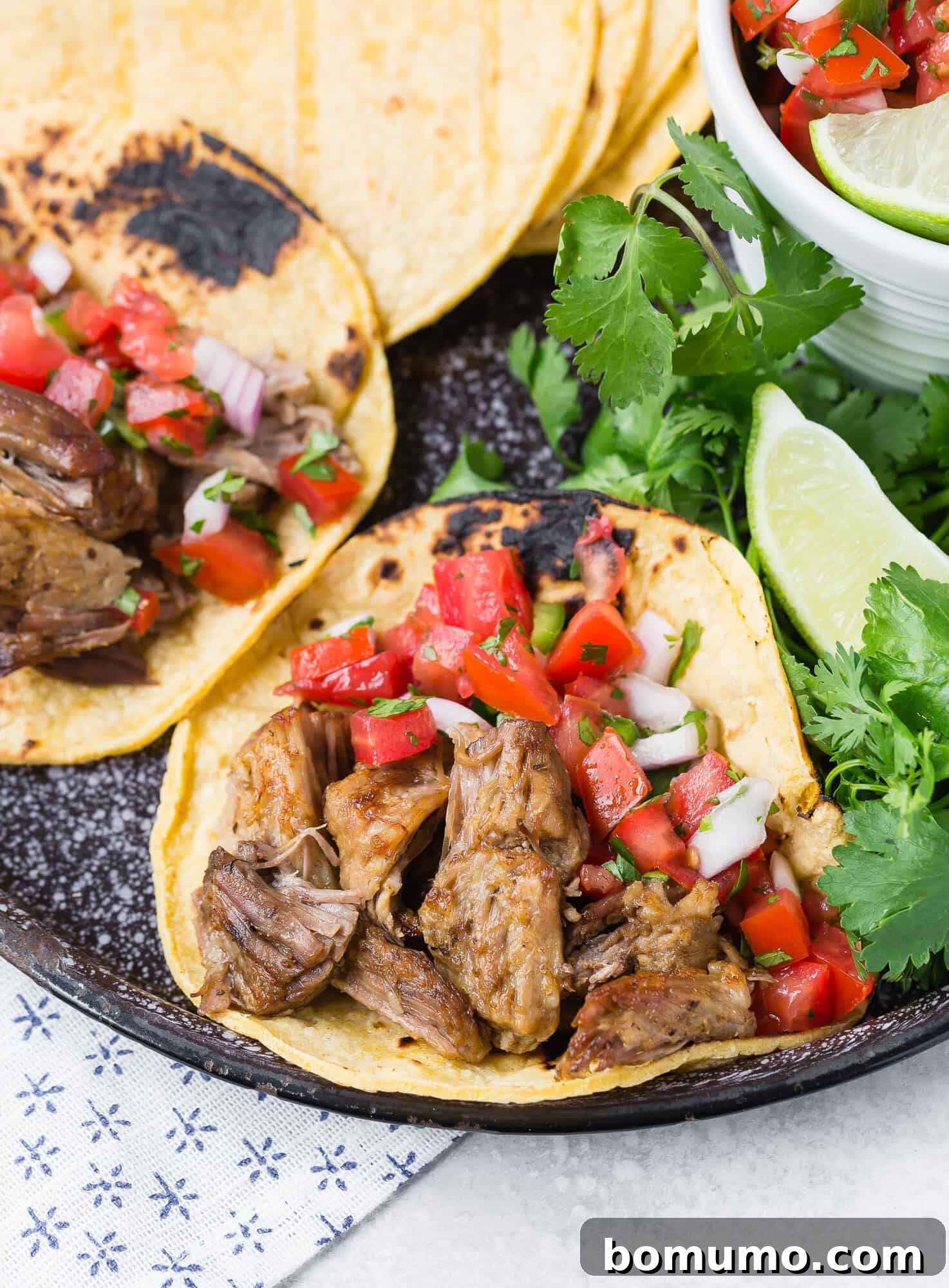 Instant pot carnitas on corn tortillas with pico de gallo, garnished with lime and cilantro, showcasing a vibrant and appetizing presentation.