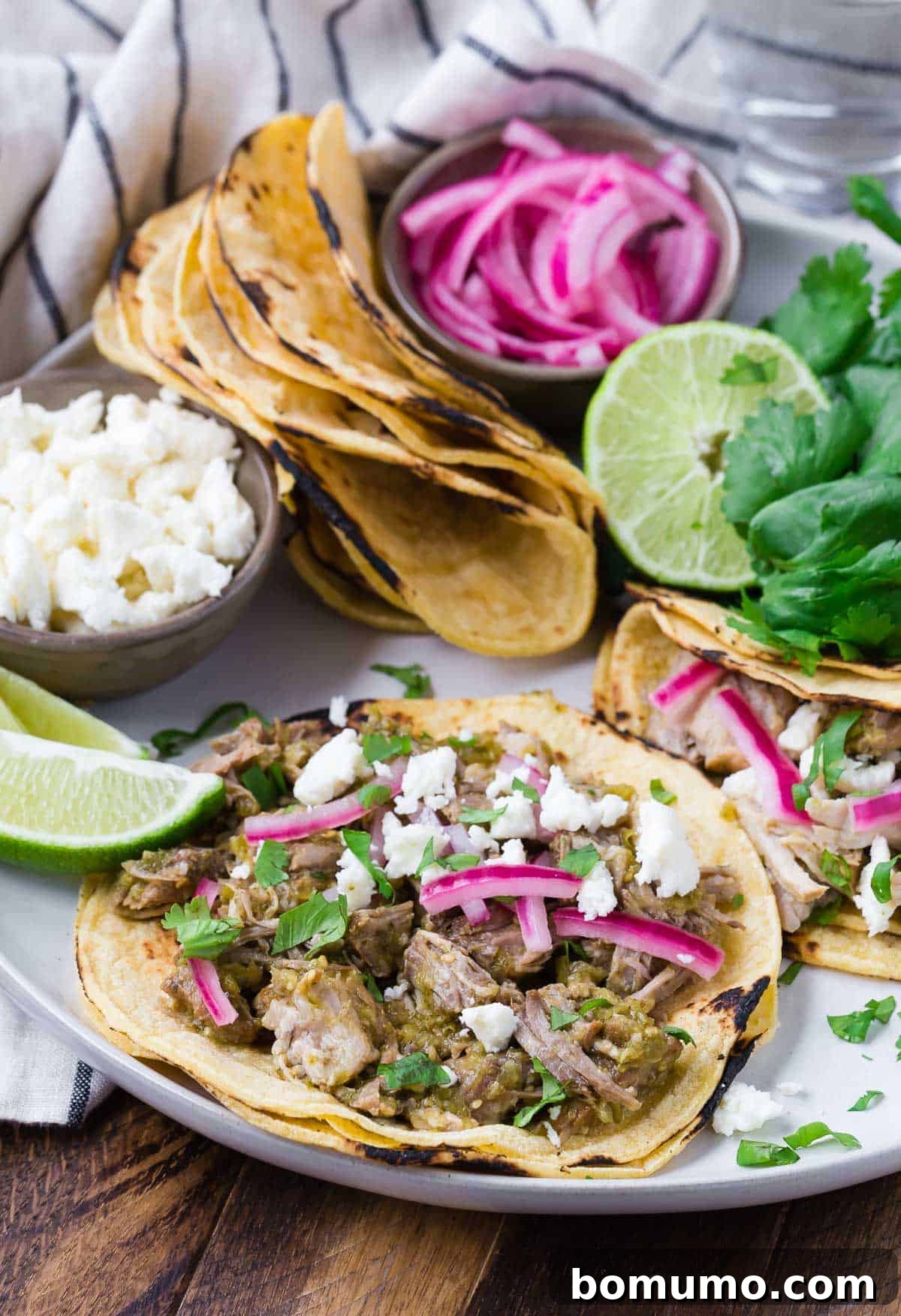 Pork verde tacos on a round platter with toppings and additional tortillas, a tempting alternative to carnitas.