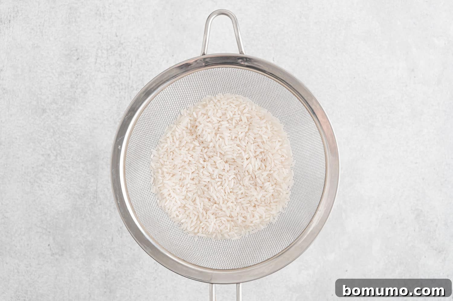 White rice being rinsed in a fine-mesh strainer under running water.