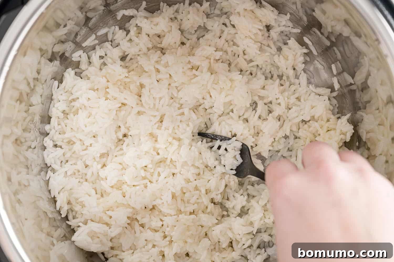 Cooked white rice being fluffed with a fork in the Instant Pot.