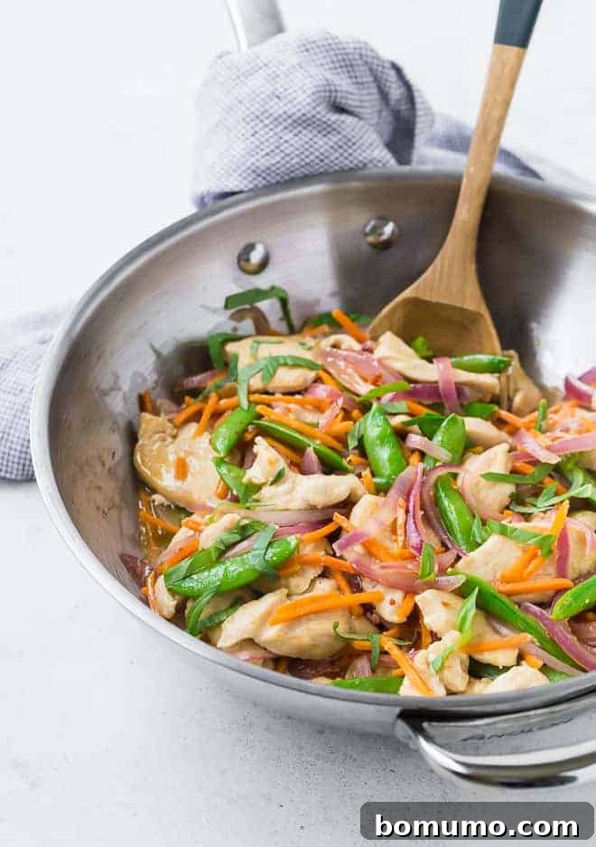 Zesty Ginger Basil Chicken 5 A beautifully cooked and colorful ginger chicken stir-fry ready in a silver wok, accompanied by a wooden spoon, showcasing a medley of fresh ingredients.