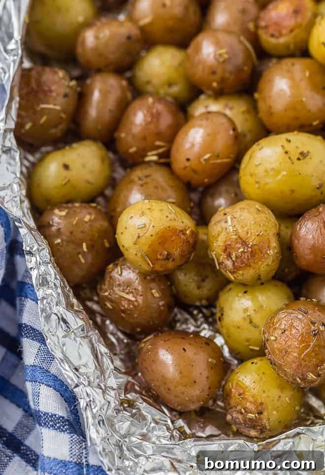 A pound and a half of baby potatoes, partially wrapped in foil. Specks of rosemary are pictured, as well as a blue and white linen.