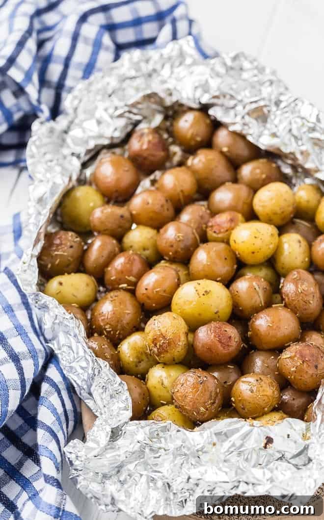 A pound and a half of baby potatoes, partially wrapped in foil. Specks of rosemary are pictured, as well as a blue and white linen.