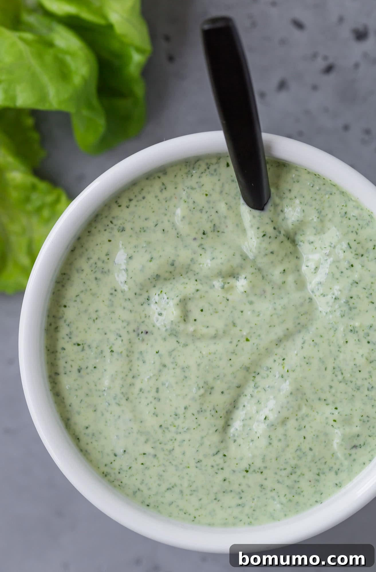 A detailed close-up shot of the vibrant green goddess dressing, presented elegantly in a pristine white bowl.