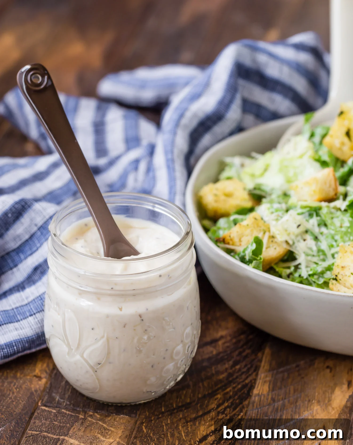 Homemade caesar salad dressing in a jar, salad in background. A delicious, healthier option for your favorite salad.