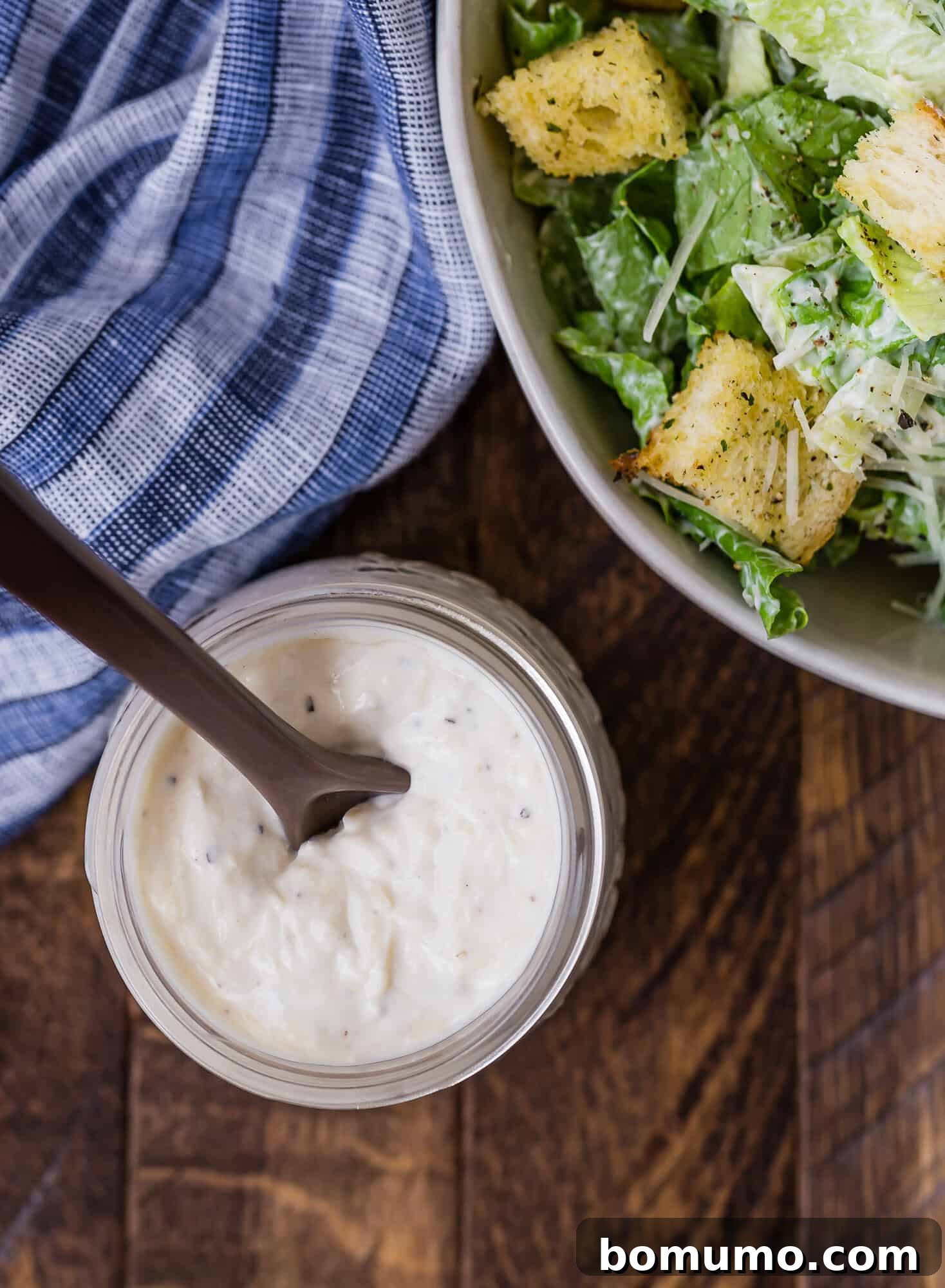 Overhead view of a jar of homemade caesar salad dressing, and a partially visible bowl of caesar salad. Ready for your next meal.