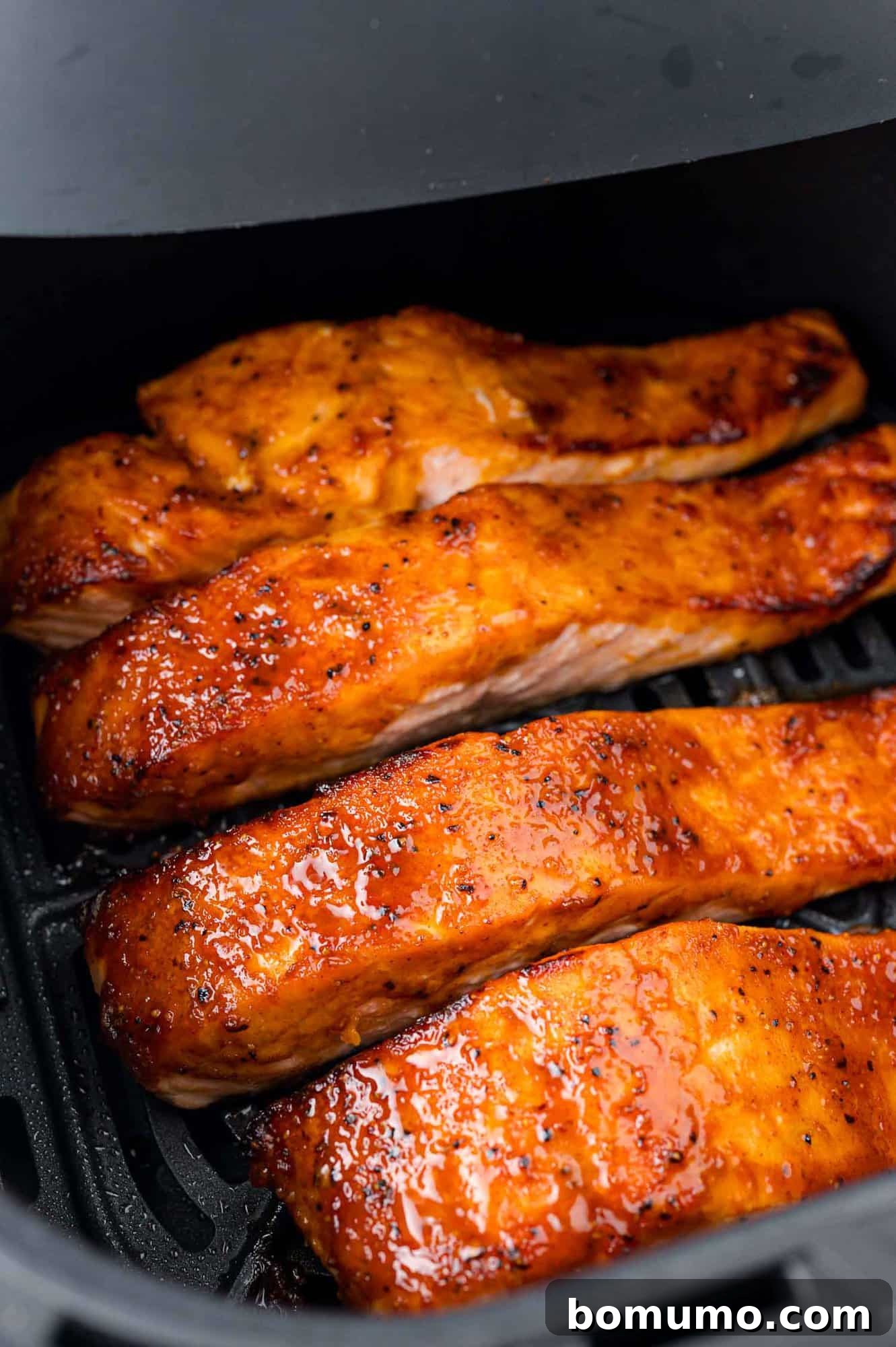 Four glazed salmon fillets in an air fryer basket, cooked to a golden brown.