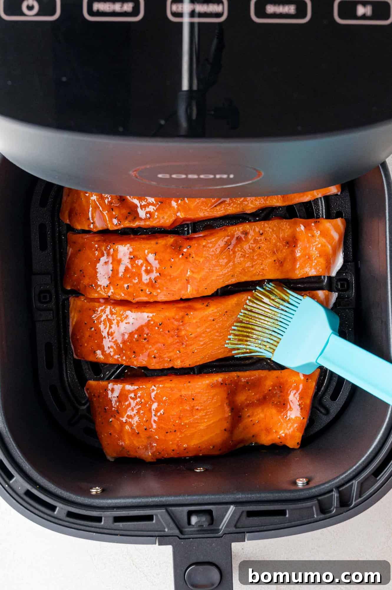 Salmon fillets brushed with glaze in an air fryer basket, ready to cook.