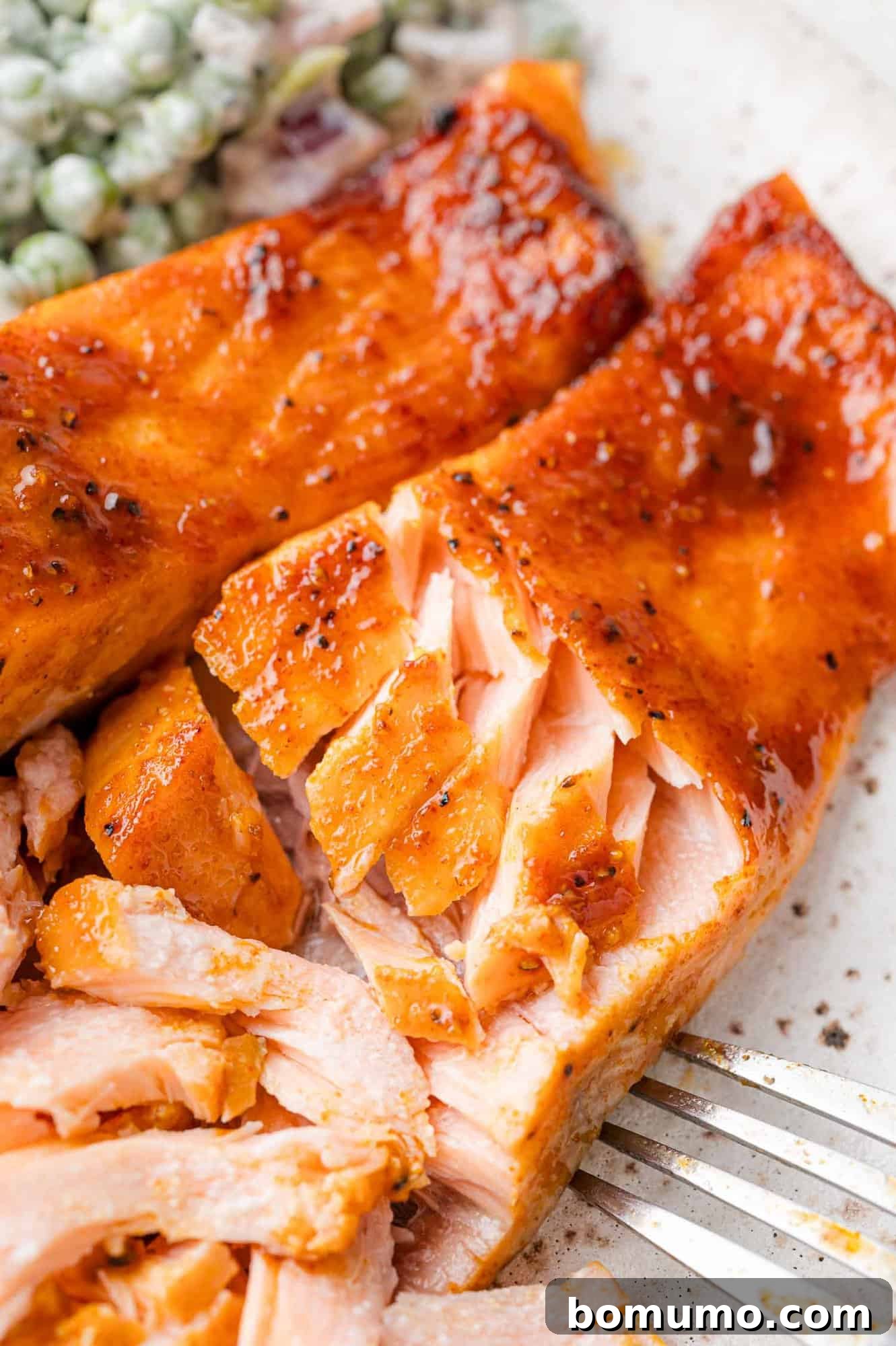 Close-up of a forked piece of cooked salmon, glazed and garnished with pepper, next to a small portion of salad.
