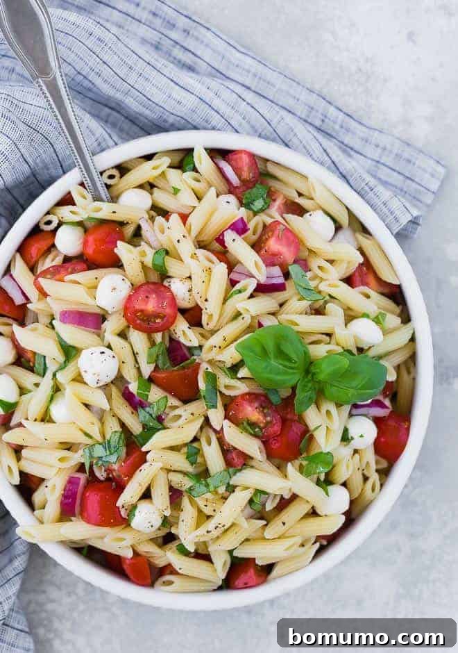 Overhead view of a bowl of pasta salad with tomatoes, fresh mozzarella, red onion, and fresh basil.