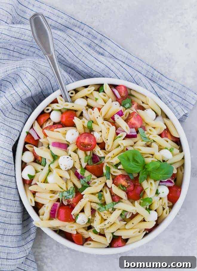 Overhead view of a bowl of pasta salad with tomatoes, fresh mozzarella, red onion, and fresh basil.
