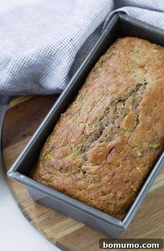 A silver loaf pan containing a freshly baked loaf of zucchini bread, resting on a rustic wooden surface.