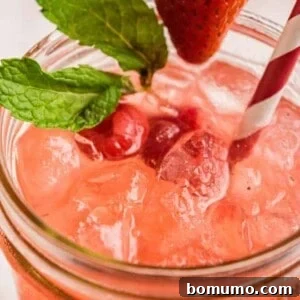 Close up view of a pink lemonade on ice, garnished with berries and fresh mint.