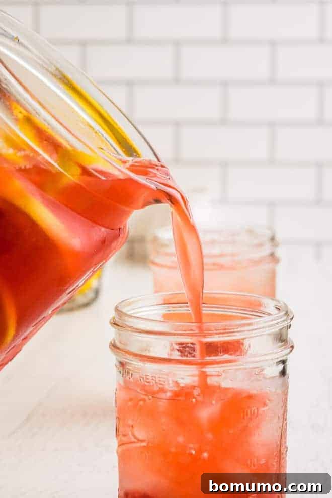 Pink lemonade being poured from a pitcher into a mason jar.
