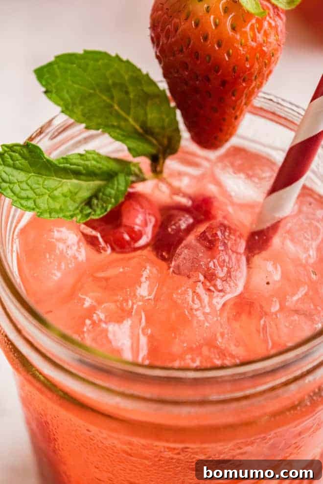 Close up view of a pink lemonade on ice, garnished with berries and fresh mint.