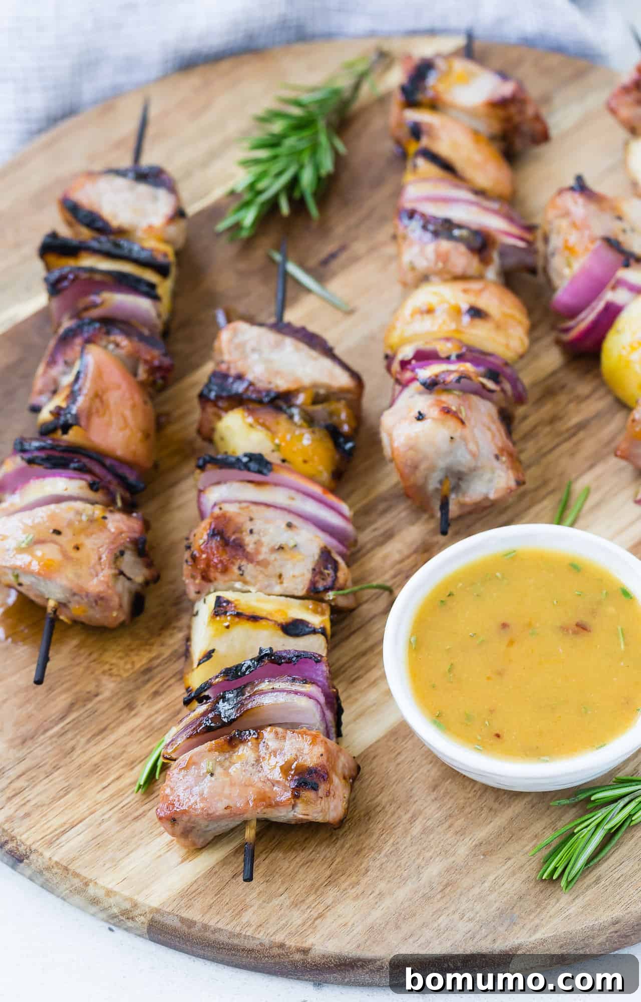 Beautifully presented pork kebobs on a wooden board, with a side of apricot dipping sauce and fresh herbs, ready for serving.