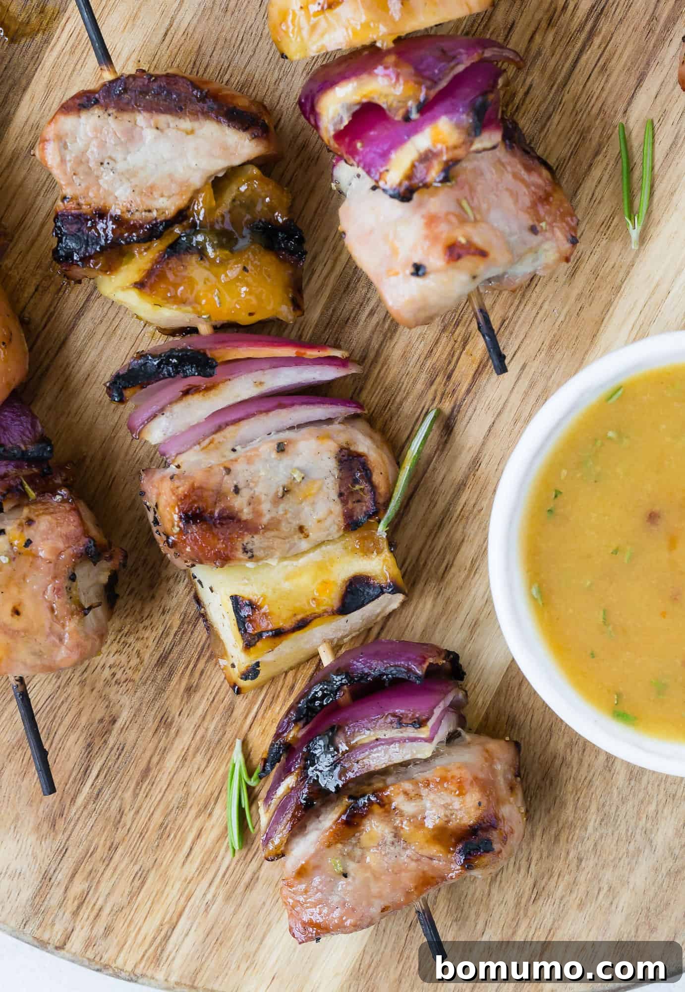 Close-up of a Grilled Pork Kabob drizzled with luscious apricot rosemary sauce, highlighting the tender pork, sweet apple, and vibrant red onion.