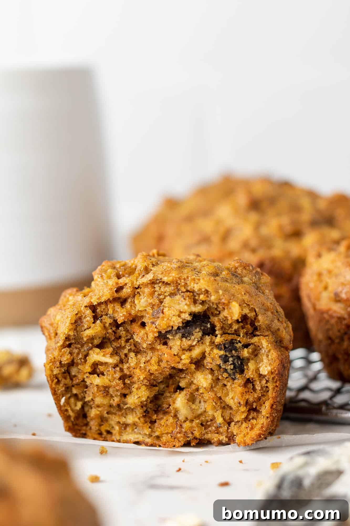 A healthy carrot raisin muffin torn in half, revealing the moist interior with visible oats, carrots, and plump raisins.