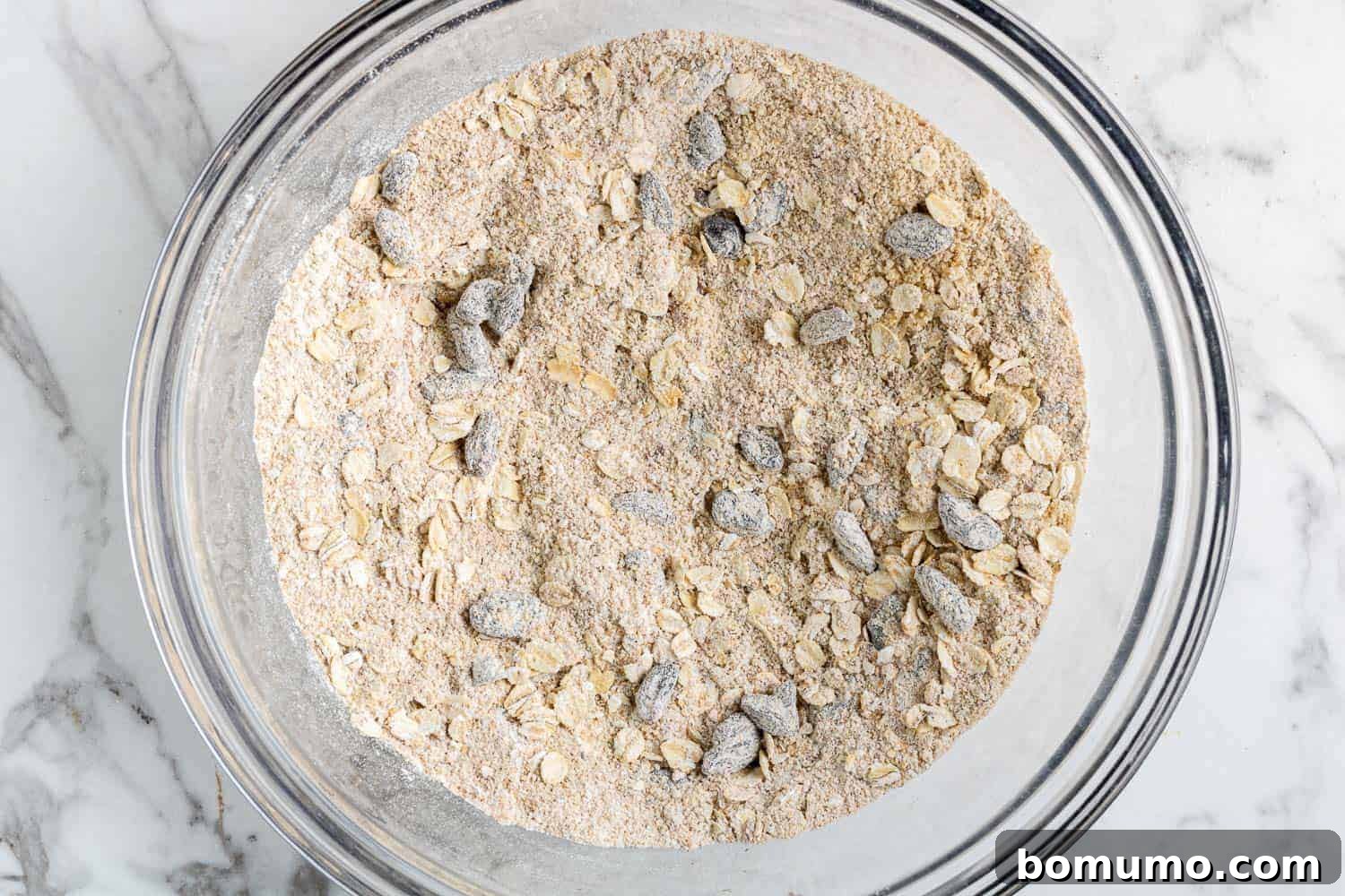 A clear glass mixing bowl filled with the whisked dry ingredients for carrot raisin muffins.