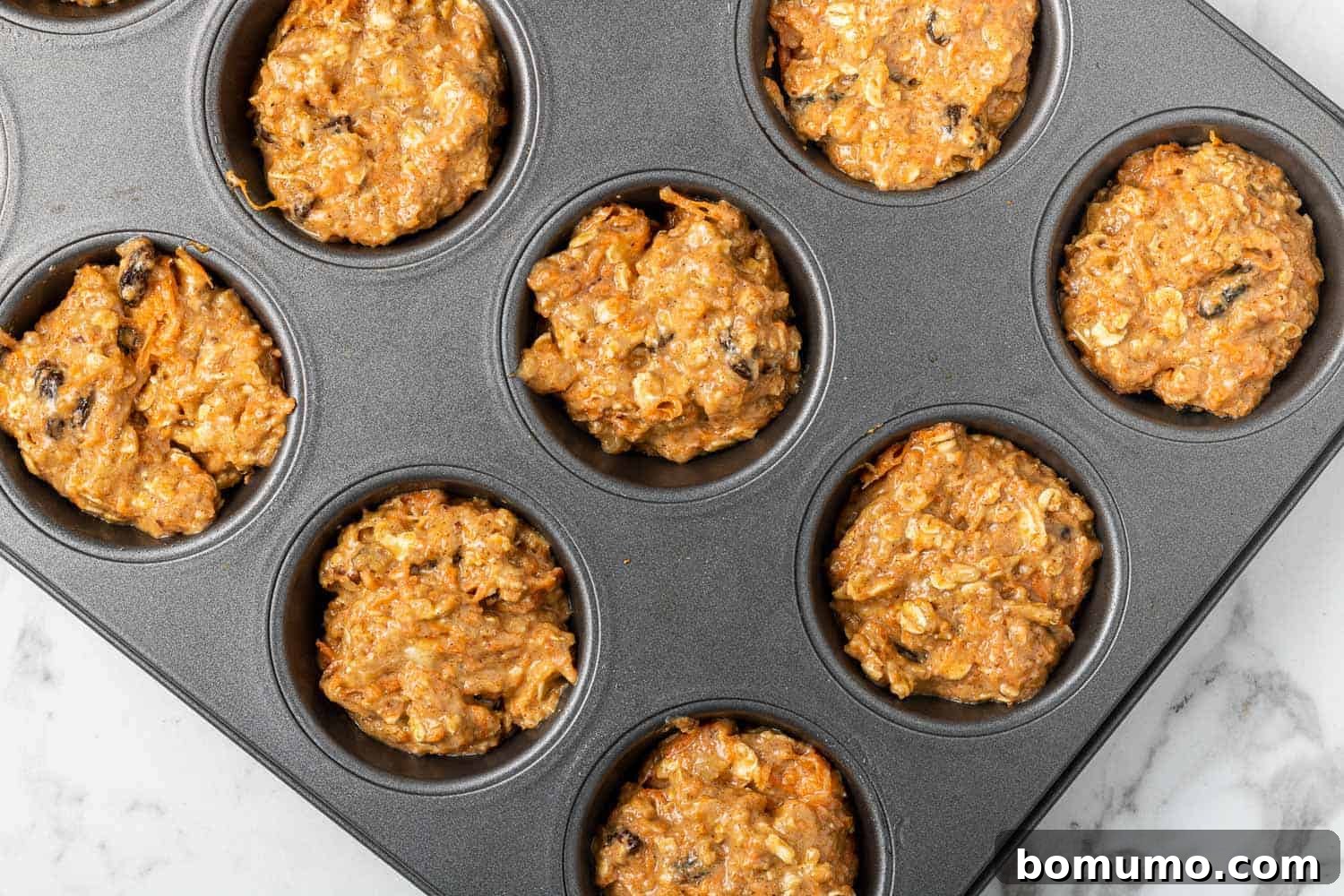 Unbaked carrot raisin muffin batter in a metal muffin tin, ready for the oven.