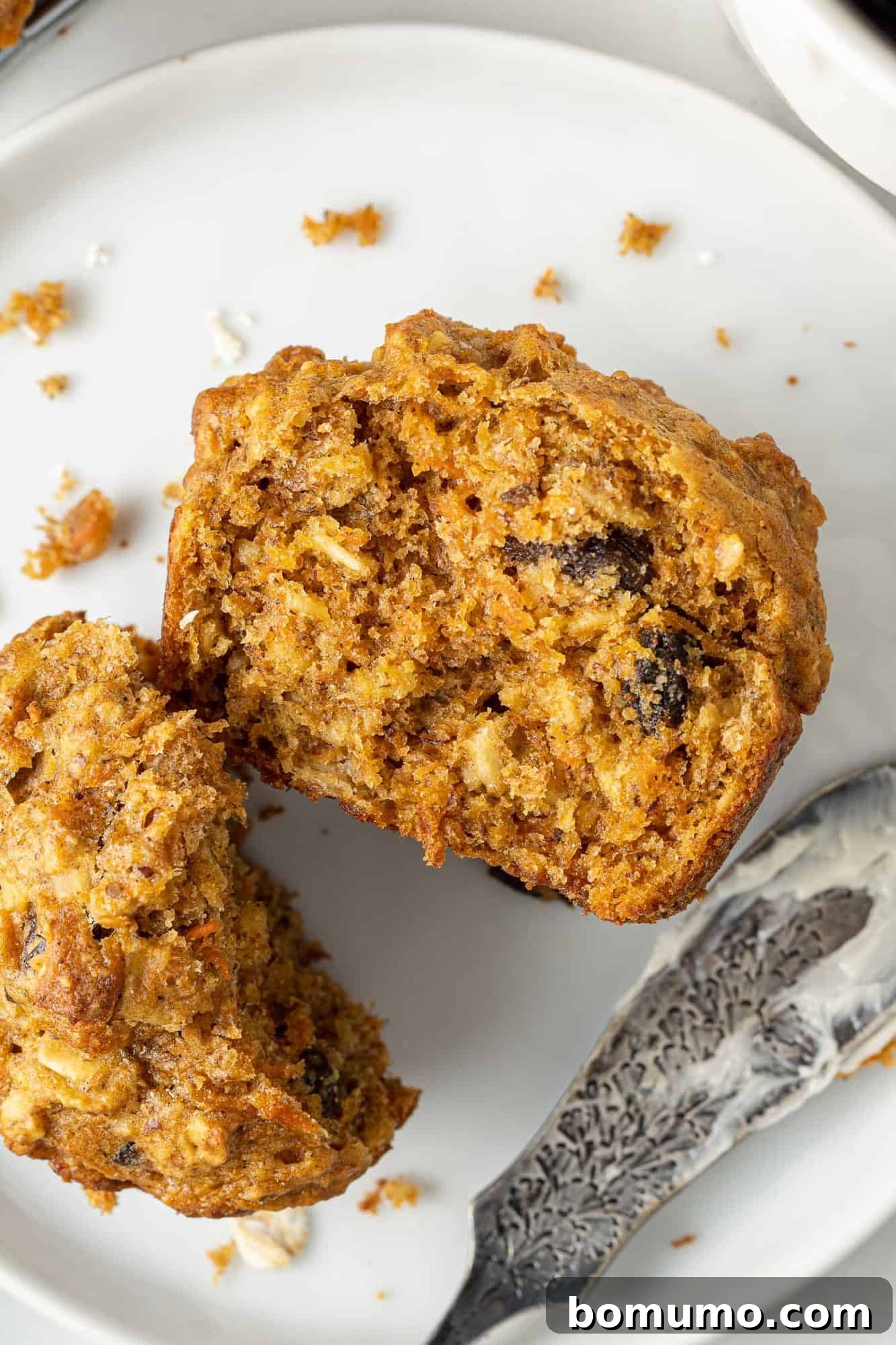A close-up shot of a carrot raisin muffin, cut in half, showcasing its moist texture and the visible pieces of carrot and raisin.