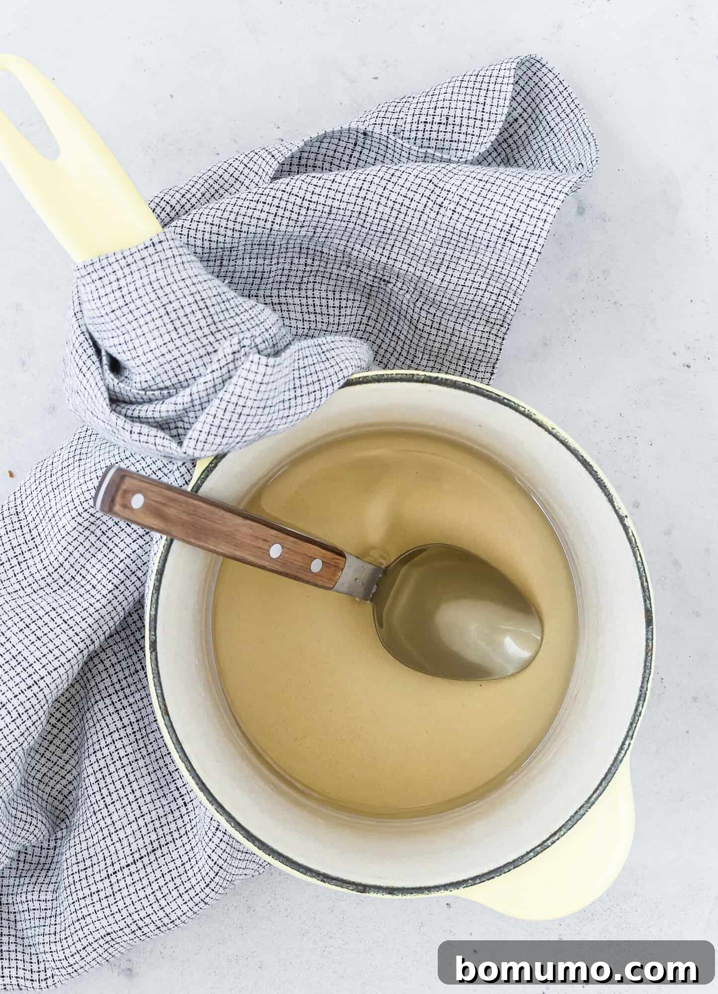 A pot of simple syrup, placed on a checked cloth on a light gray surface, perfectly illustrating its readiness for use.