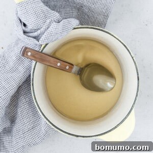 A pot of simple syrup with a wooden-handled spoon on a checkered cloth background.