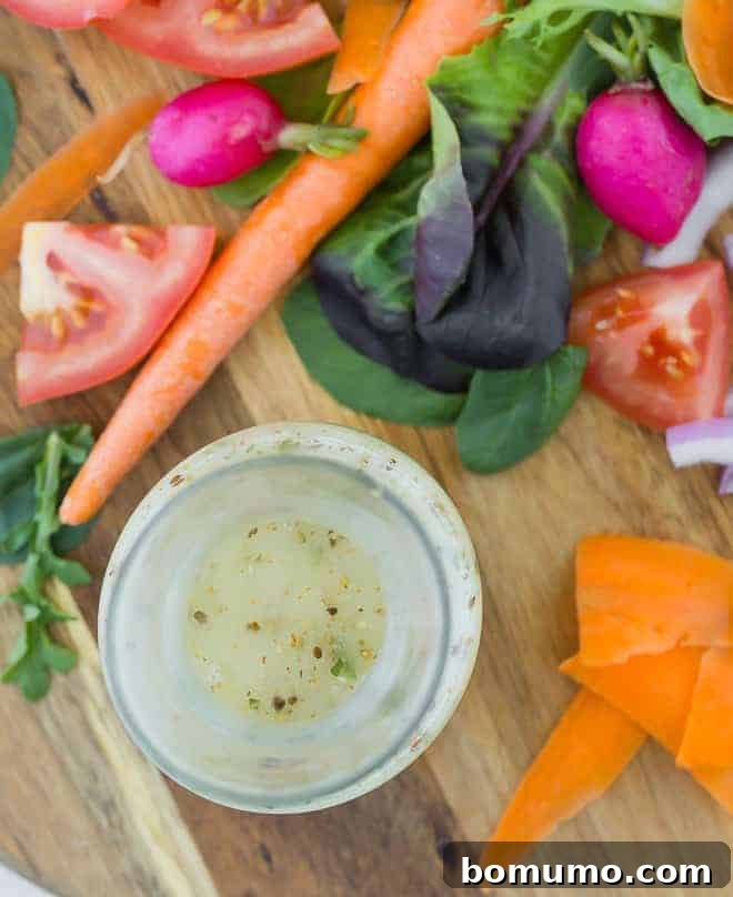 Authentic Italian Dressing from Scratch 3 Overhead view of Italian dressing in a small glass bottle, surrounded by fresh vegetables on a wooden cutting board.