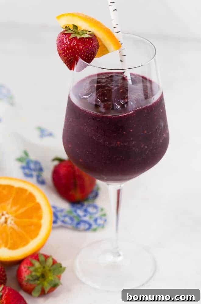 Refreshing Sangria Slushie 3 A single elegant long-stemmed wine glass filled with a ruby-red frozen sangria slushie, adorned with a fresh strawberry and a vibrant orange slice. A stylish paper straw completes the refreshing presentation.