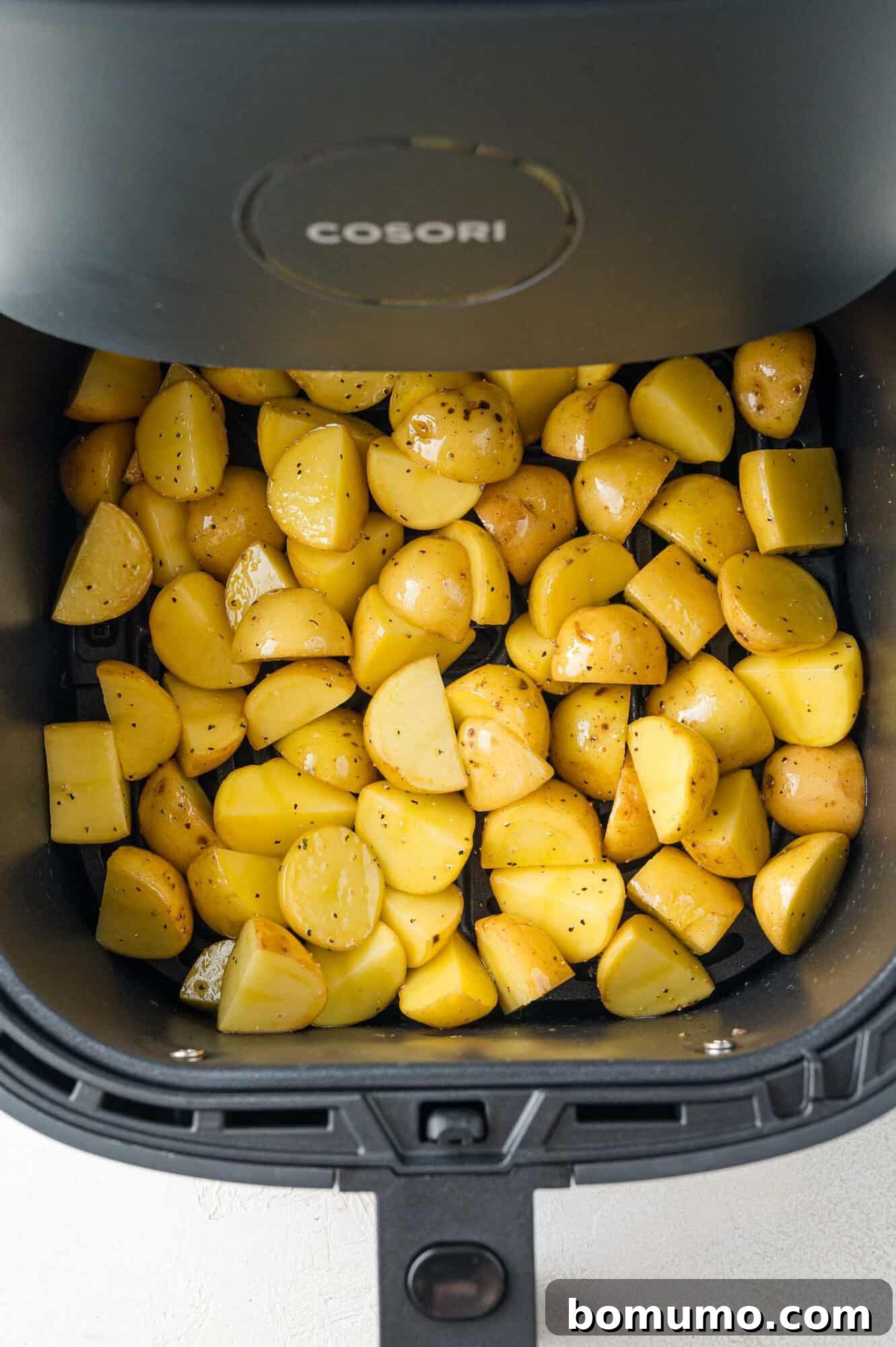Halved baby potatoes are neatly arranged in the air fryer basket, uncooked and ready for the air frying process.