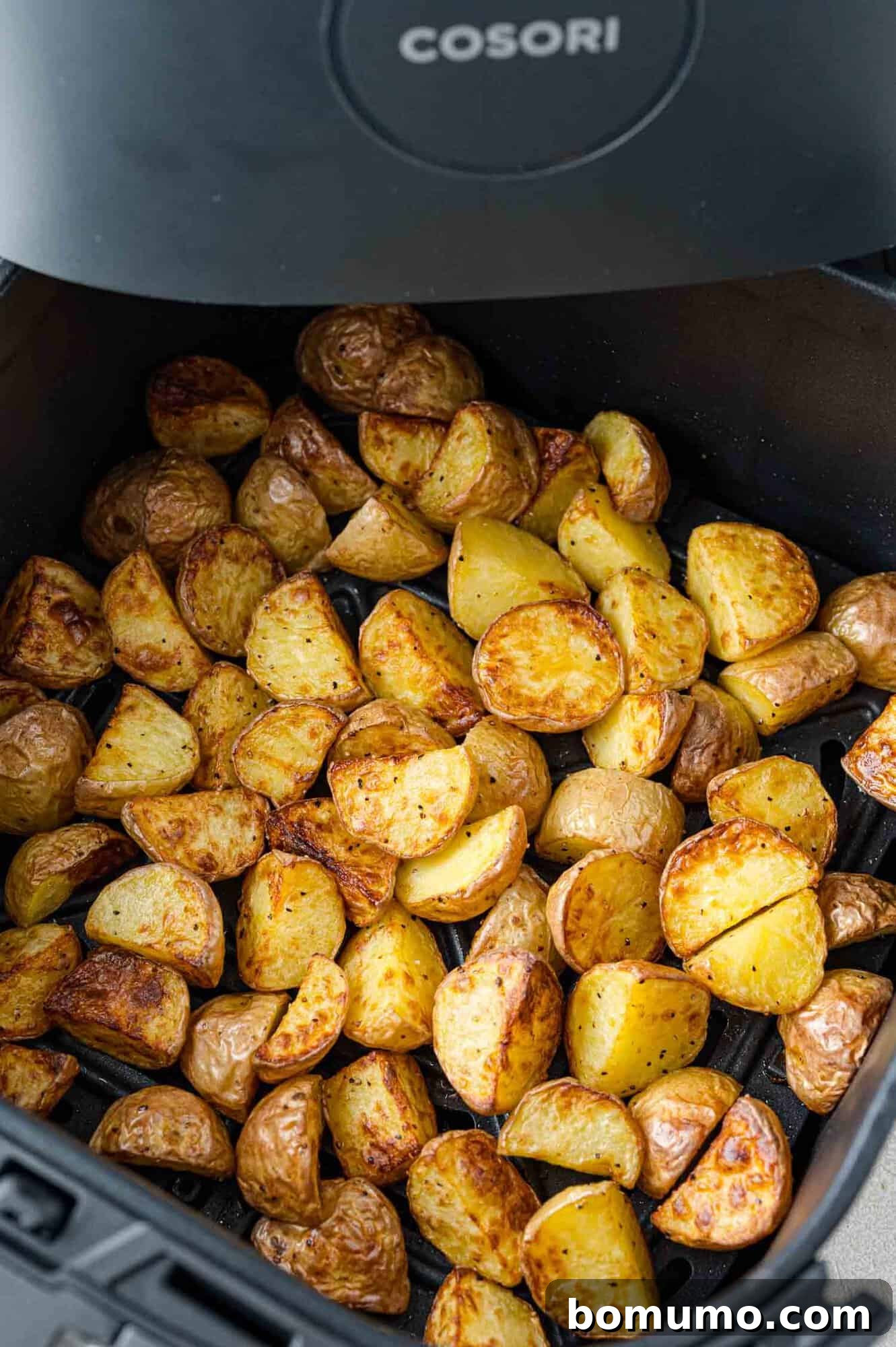 Golden-brown, perfectly cooked halved baby potatoes are shown in the air fryer basket immediately after cooking, looking delightfully crispy.