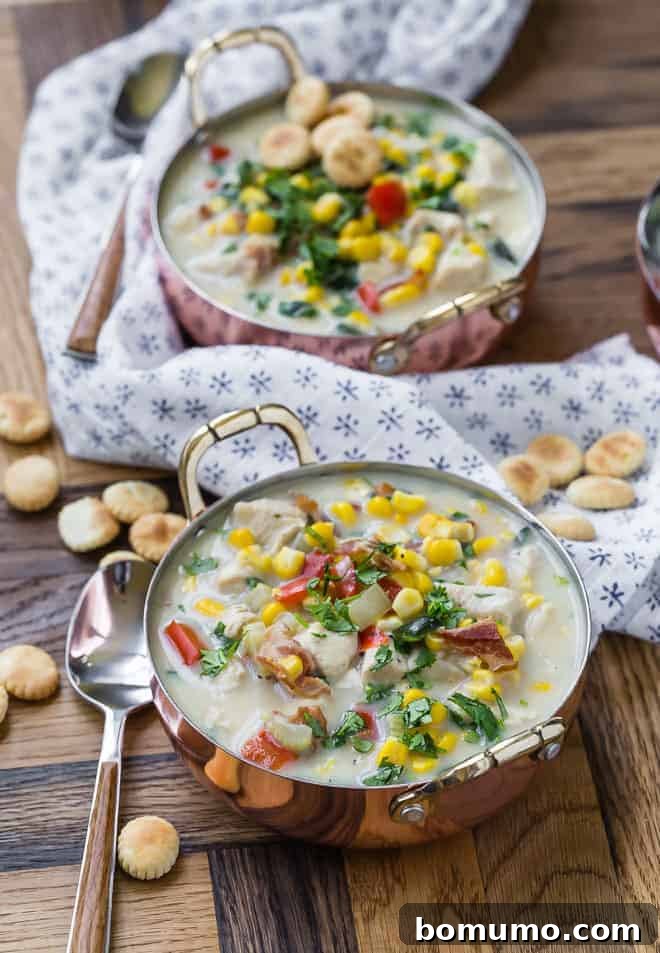 Wholesome Chicken Corn Chowder 4 Two bowls of golden corn chowder in rustic copper bowls, alongside a blue and white linen napkin and a scattering of oyster crackers, ready to be served.