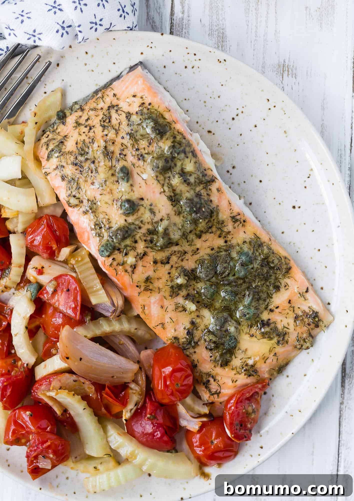 A perfectly plated portion of cooked salmon with roasted tomatoes and fennel, elegantly garnished with fresh herbs.