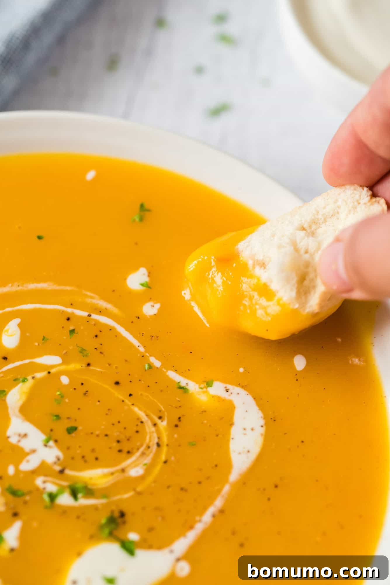 A hand dips a piece of bread into a bowl of pumpkin soup.