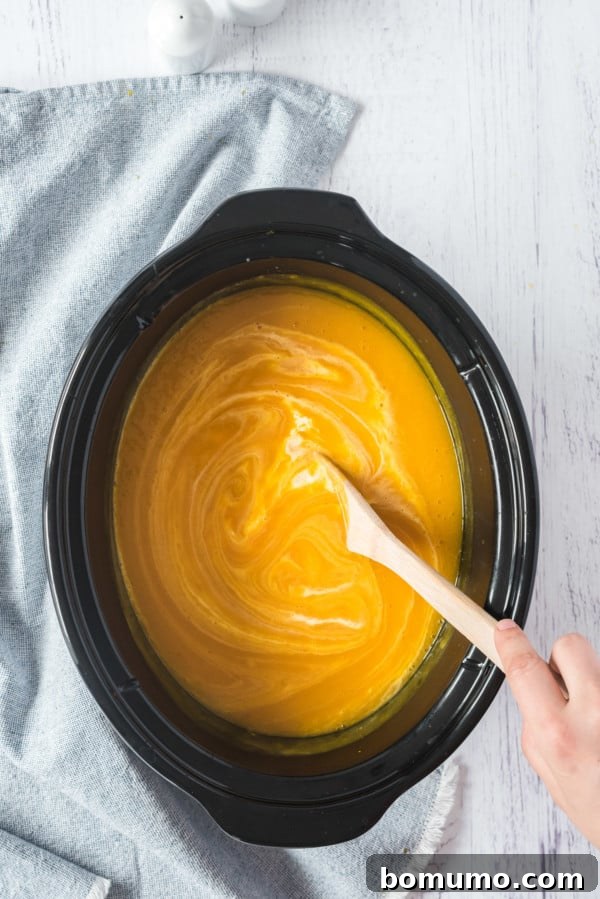 Cream being stirred into pumpkin soup inside the slow cooker.