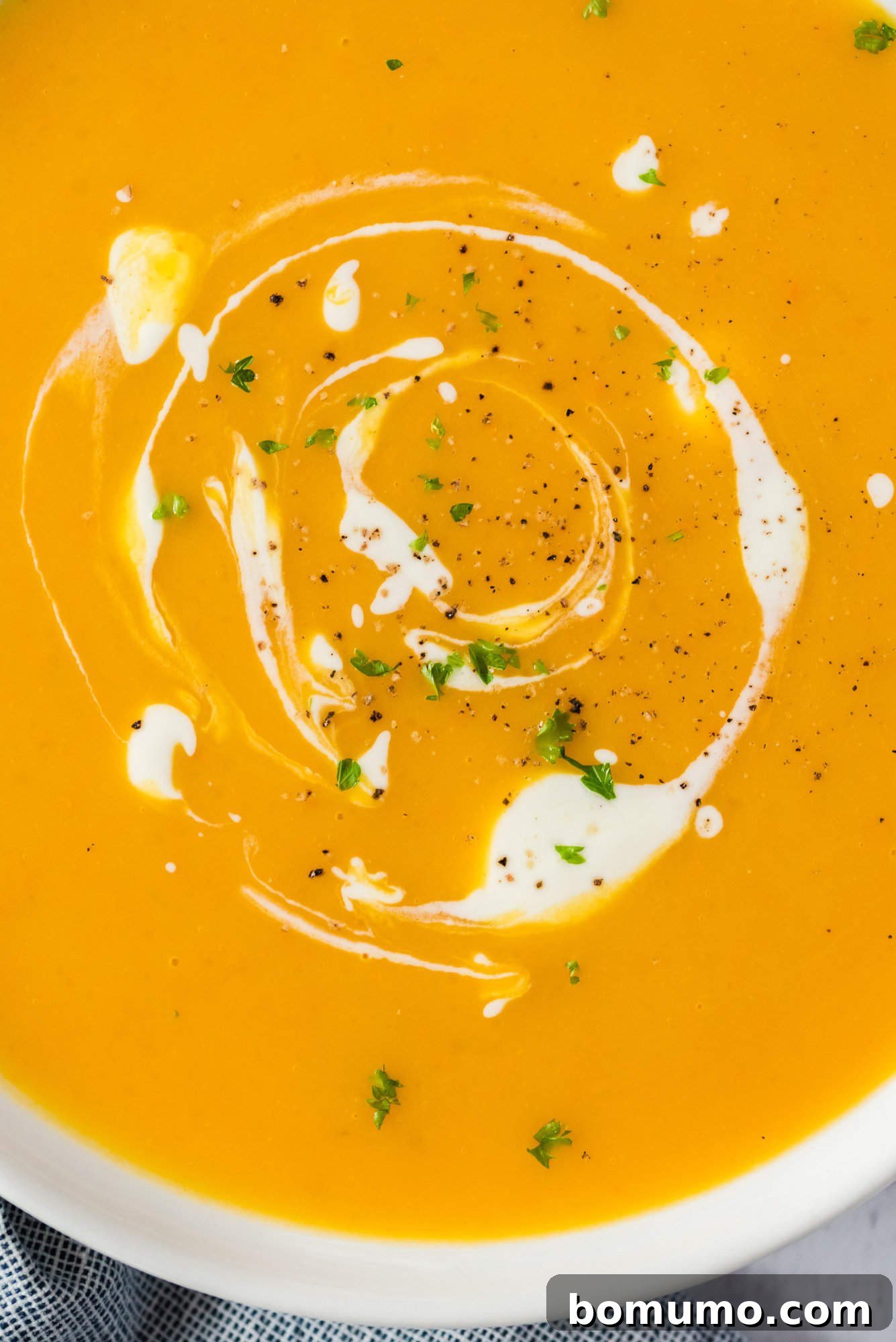 Close up overhead view of pumpkin soup in a bowl with a swirl of cream.