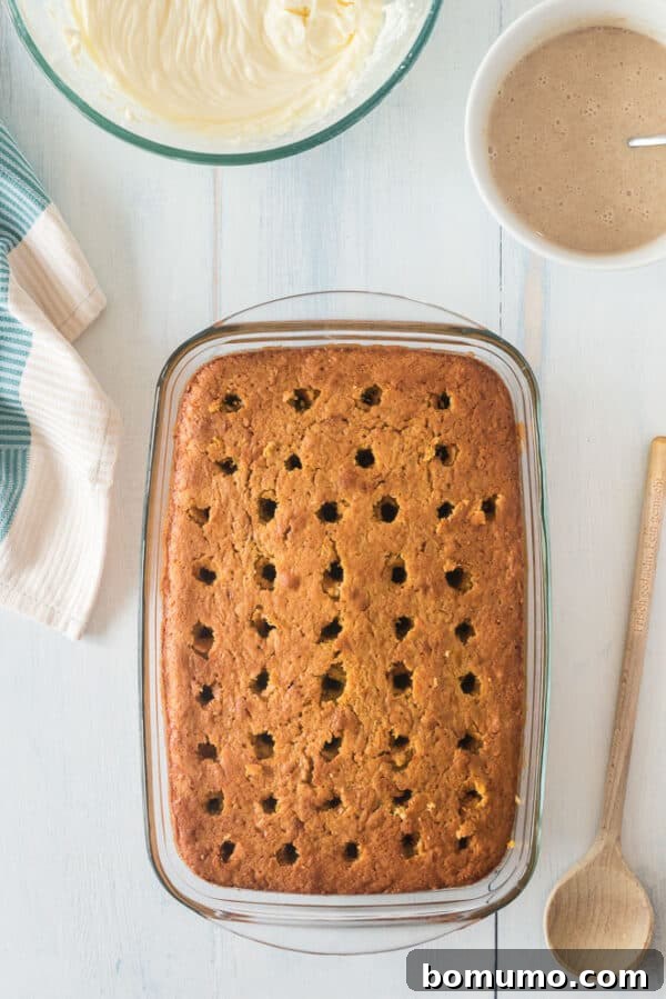 This pumpkin poke cake recipe is an easy fall dessert oozing with sweet cinnamon filling and smothered with tangy cream cheese frosting. Pumpkin cake covered with holes on a countertop.