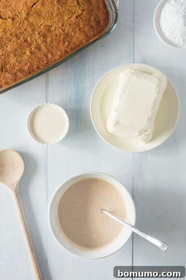 This pumpkin poke cake recipe is an easy fall dessert oozing with sweet cinnamon filling and smothered with tangy cream cheese frosting. Cinnamon condensed milk in a bowl for the poke cake filling, next to a baked cake and more ingredients.