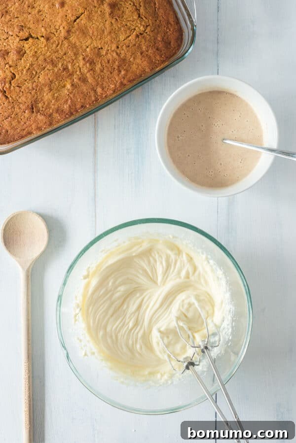 This pumpkin poke cake recipe is an easy fall dessert oozing with sweet cinnamon filling and smothered with tangy cream cheese frosting. Cream cheese frosting ingredients combined in a bowl next to a smaller bowl of cinnamon condensed milk and a baked pumpkin cake.