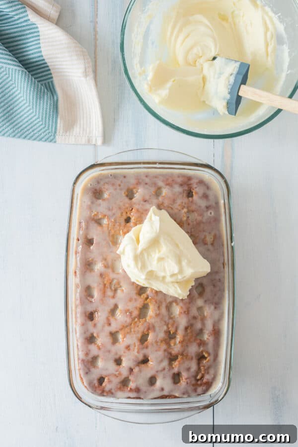 This pumpkin poke cake recipe is an easy fall dessert oozing with sweet cinnamon filling and smothered with tangy cream cheese frosting. A dollop of cream cheese frosting on top of a pumpkin poke cake.