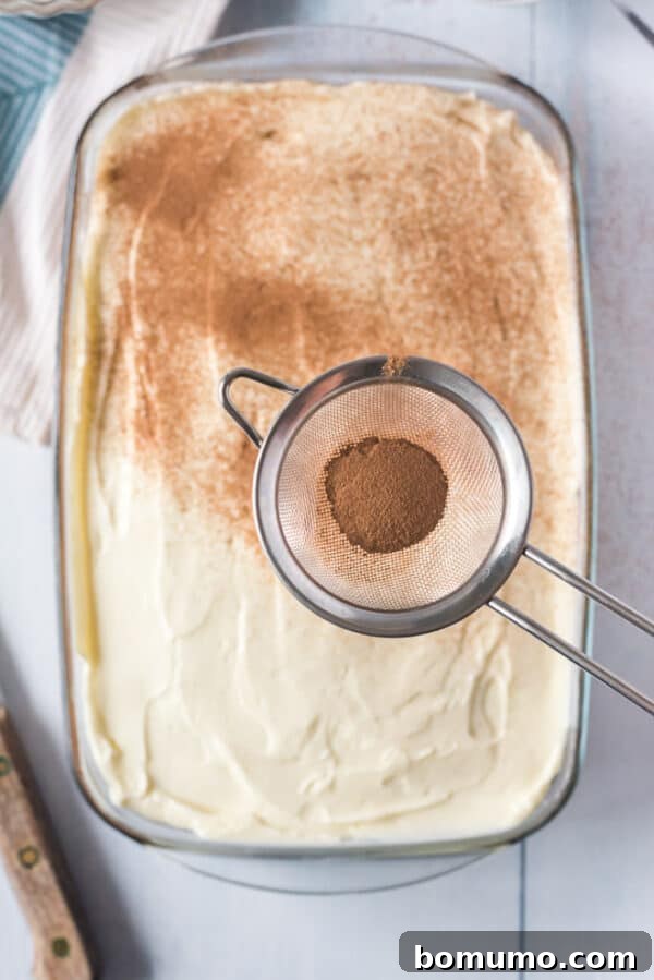 This pumpkin poke cake recipe is an easy fall dessert oozing with sweet cinnamon filling and smothered with tangy cream cheese frosting. Cinnamon being sifted over a frosted pumpkin poke cake.
