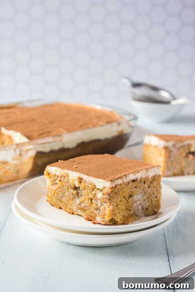 This pumpkin poke cake recipe is an easy fall dessert oozing with sweet cinnamon filling and smothered with tangy cream cheese frosting. Pumpkin poke cake on a white plate, more cake in the background.