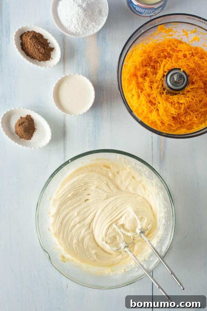 This pumpkin poke cake recipe is an easy fall dessert oozing with sweet cinnamon filling and smothered with tangy cream cheese frosting. Pumpkin poke cake batter ingredients combined in a bowl using a hand mixer, surrounded by more ingredients on a countertop.