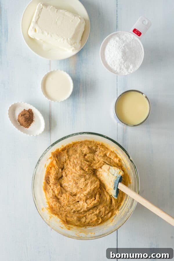 This pumpkin poke cake recipe is an easy fall dessert oozing with sweet cinnamon filling and smothered with tangy cream cheese frosting. Pumpkin poke cake batter in a bowl next to more ingredients on a countertop.