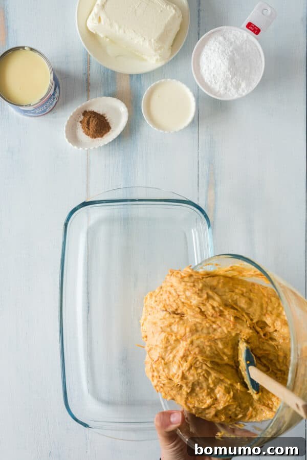 This pumpkin poke cake recipe is an easy fall dessert oozing with sweet cinnamon filling and smothered with tangy cream cheese frosting. Pumpkin poke cake batter poured into a 9x13-inch cake pan.