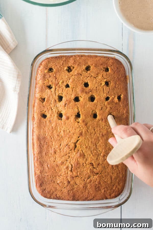 This pumpkin poke cake recipe is an easy fall dessert oozing with sweet cinnamon filling and smothered with tangy cream cheese frosting. Holes being poked in a baked pumpkin cake with a wooden spoon handle.