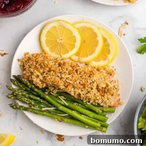 Overhead view of almond and parmesan crusted salmon on a plate with lemon slices and asparaugs.