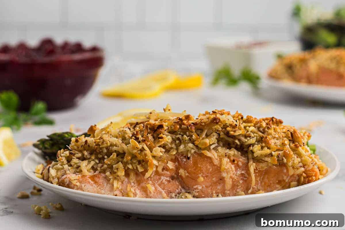 A close-up view of perfectly cooked salmon on a white plate, showcasing its golden, crispy almond and Parmesan cheese crust and moist, flaky interior.