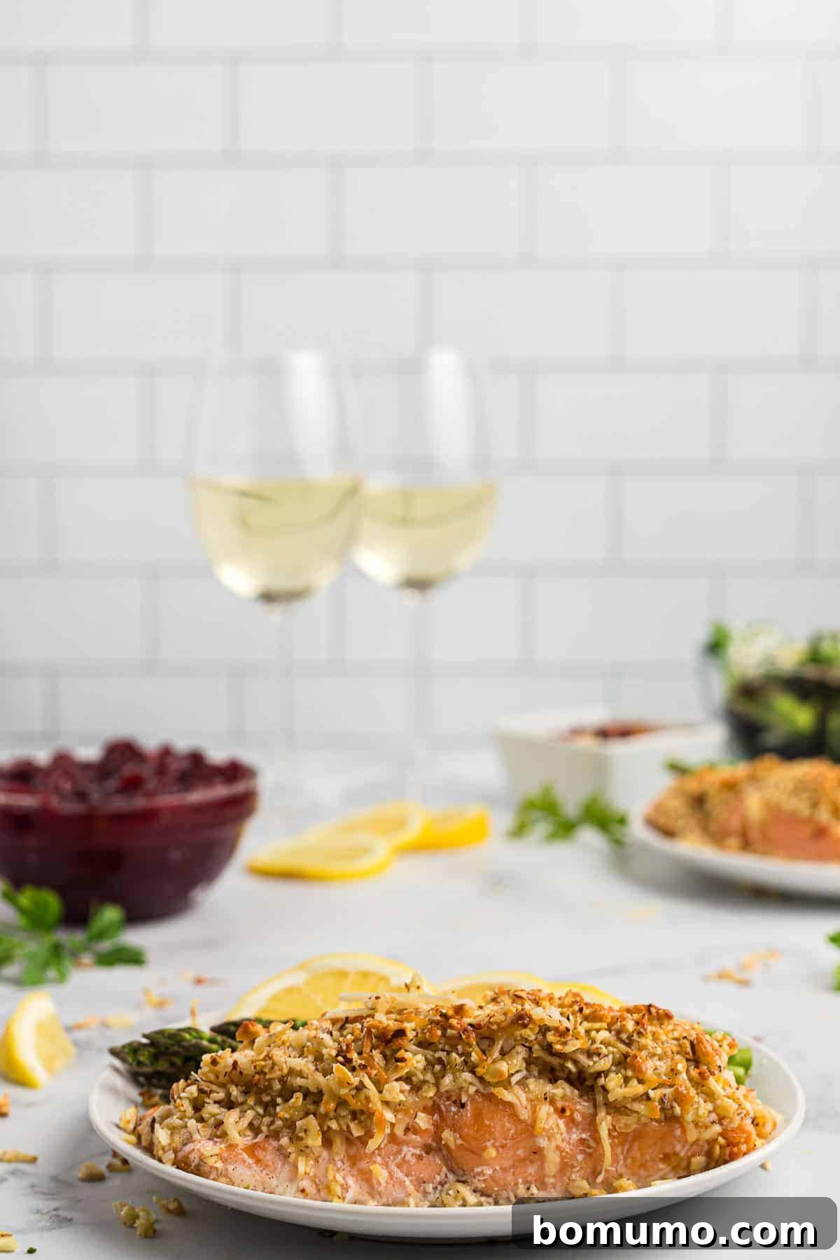 A beautifully plated almond and Parmesan crusted salmon dinner, complete with a glass of white wine and additional complementary dishes subtly blurred in the background, creating an inviting meal scene.