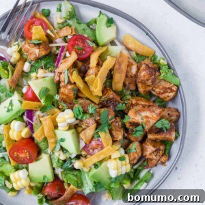 Overhead view of a colorful chopped salad on a grey plate. Salad includes bbq grilled chicken, lettuce, onion, tomato, crispy tortilla strips, avocado, corn and more!